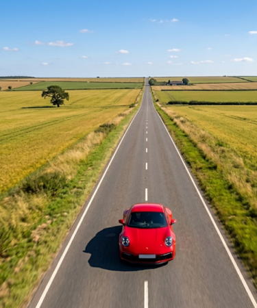 Opony letnie w czerwony Porsche mknącym prostą drogą wśród pól