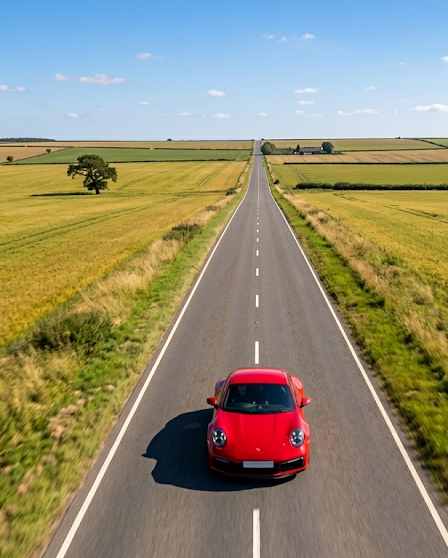 Opony letnie w czerwony Porsche mknącym prostą drogą wśród pól